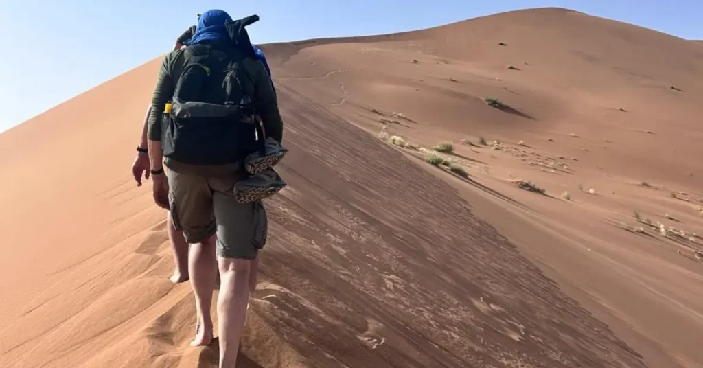 Morocco travel group trekking barefoot over golden sand dunes