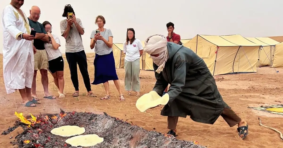 Nomad guide baking desert bread in fire pit as Morocco travel group watches