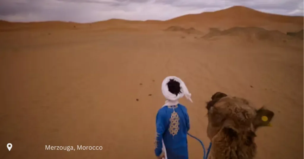 Man in traditional clothing leading a camel through the Sahara dunes in Merzouga